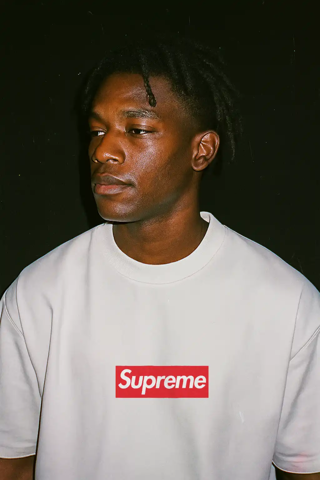 AI Photoshoot Recipe: Lo-Fi Flash Portrait on Black - Mock It AI Man with dreadlocks wearing white Supreme t-shirt on black background.